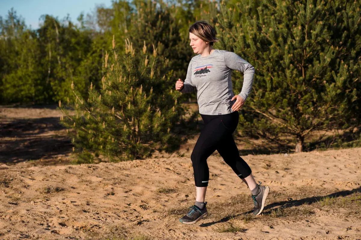 Frau beim **trail running** auf sandigem Untergrund, umgeben von Kiefern und Bäumen.