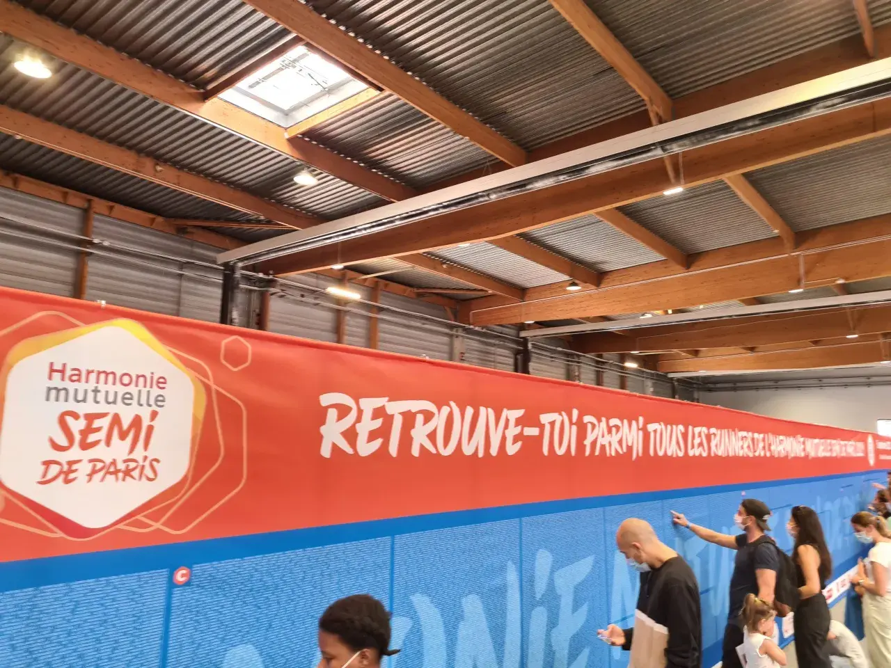 Harmonie Mutuelle SEMI DE PARIS Banner. Menschen stehen vor einer Wand mit Namen, die für den Lauf des SEMI DE PARIS werben.