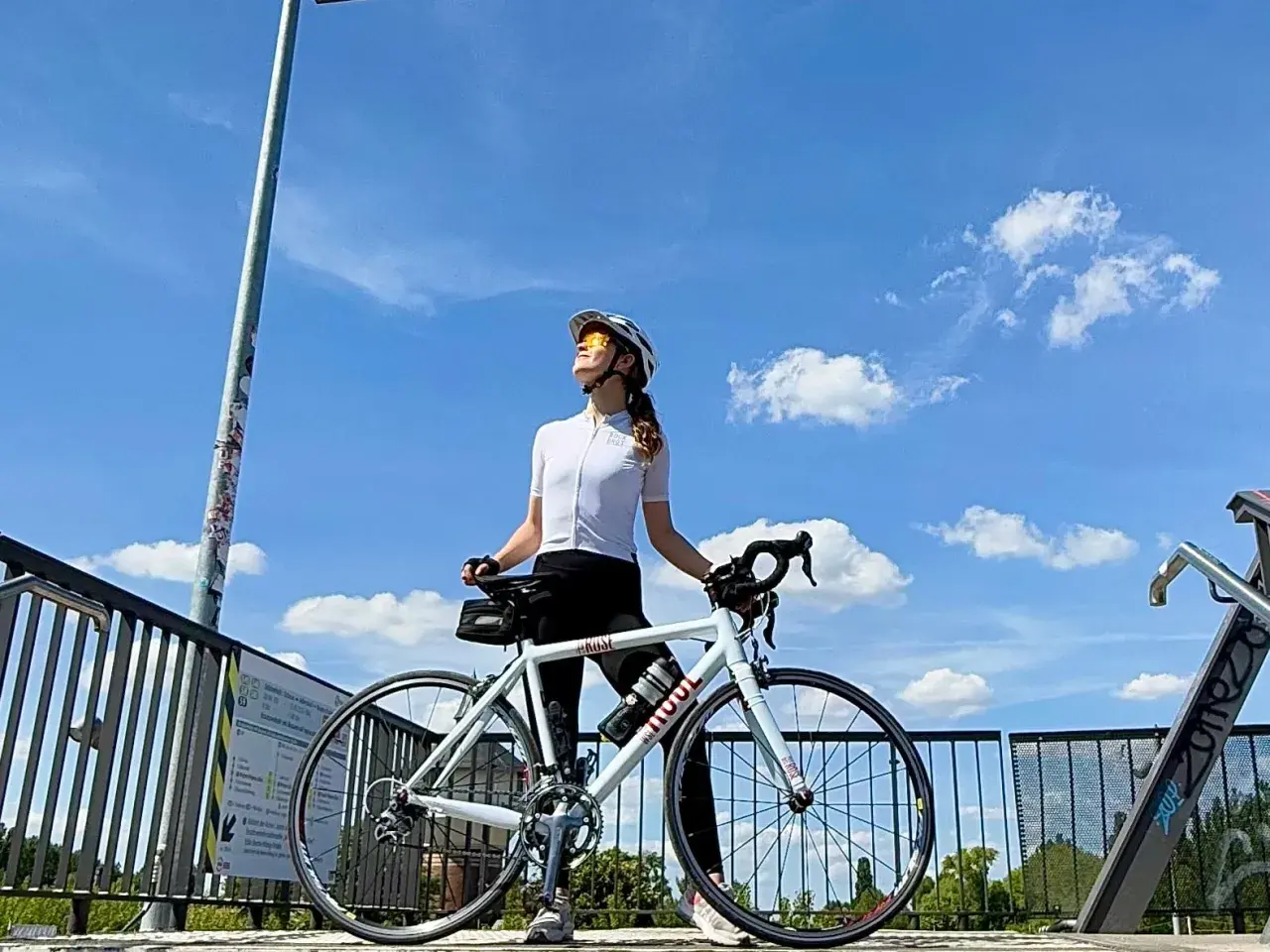 Frau mit Rennrad genießt die Sonne nach einem intensiven Intervalltraining Fahrrad. Blauer Himmel mit Wolken.