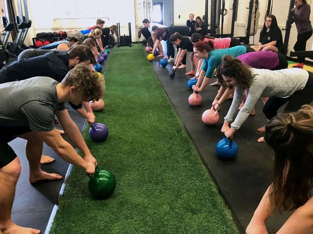 Gruppe von Menschen in einer Fitnesshalle, die Kettlebell-&Uuml;bungen machen. Die sportliche Motivation ist sp&uuml;rbar, w&auml;hrend sie sich auf ihre Gewichte konzentrieren.