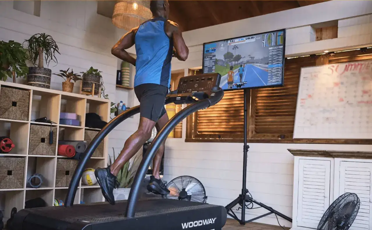Mann l&auml;uft auf Laufband, w&auml;hrend er einen virtuellen Lauf auf einem Bildschirm verfolgt.