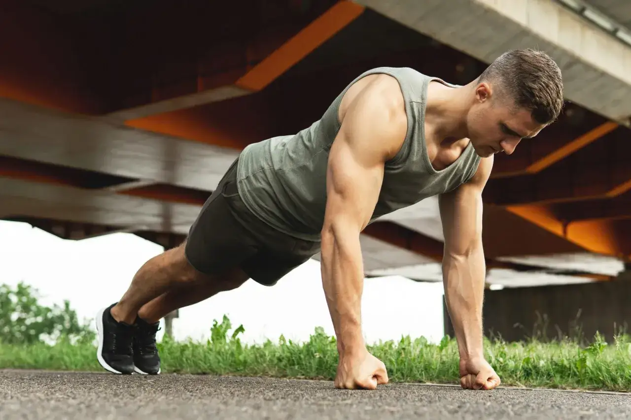 Ein Mann macht Liegest&uuml;tze unter einer Br&uuml;cke. Sein K&ouml;rper ist angespannt, ein Zeichen f&uuml;r seinen intensiven Calisthenics Trainingsplan.