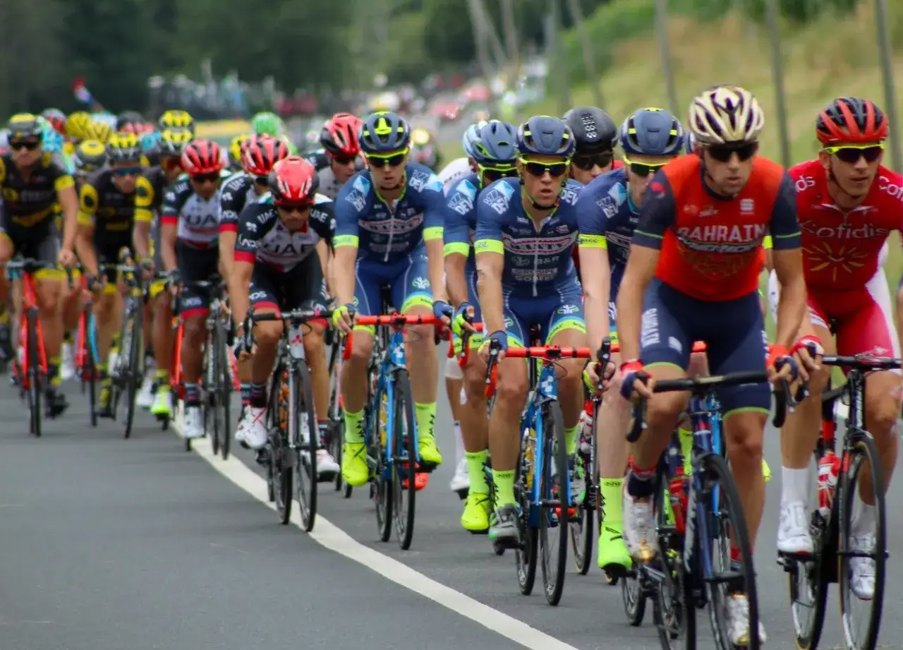 Eine Gruppe von Radfahrern, die an einer Tour de France teilnehmen. Man sieht viele Fahrer in voller Fahrt, die um die F&uuml;hrung k&auml;mpfen.