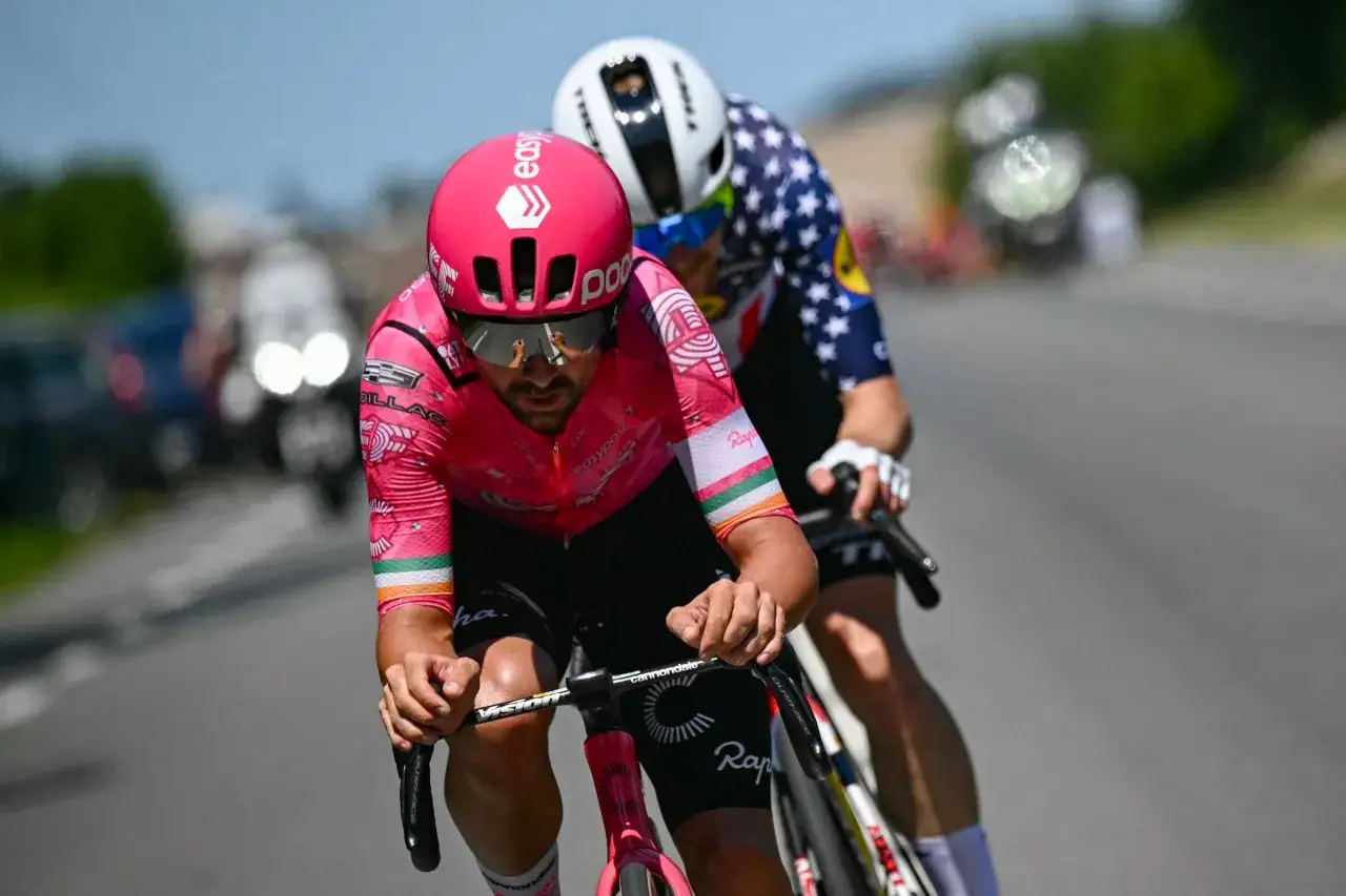 Zwei Radprofis im Rennen, einer in Pink, der andere mit Sternenmuster. Lange Socken sind ein Muss, warum tragen rennradfahrer lange socken? Aerodynamik und Schutz.