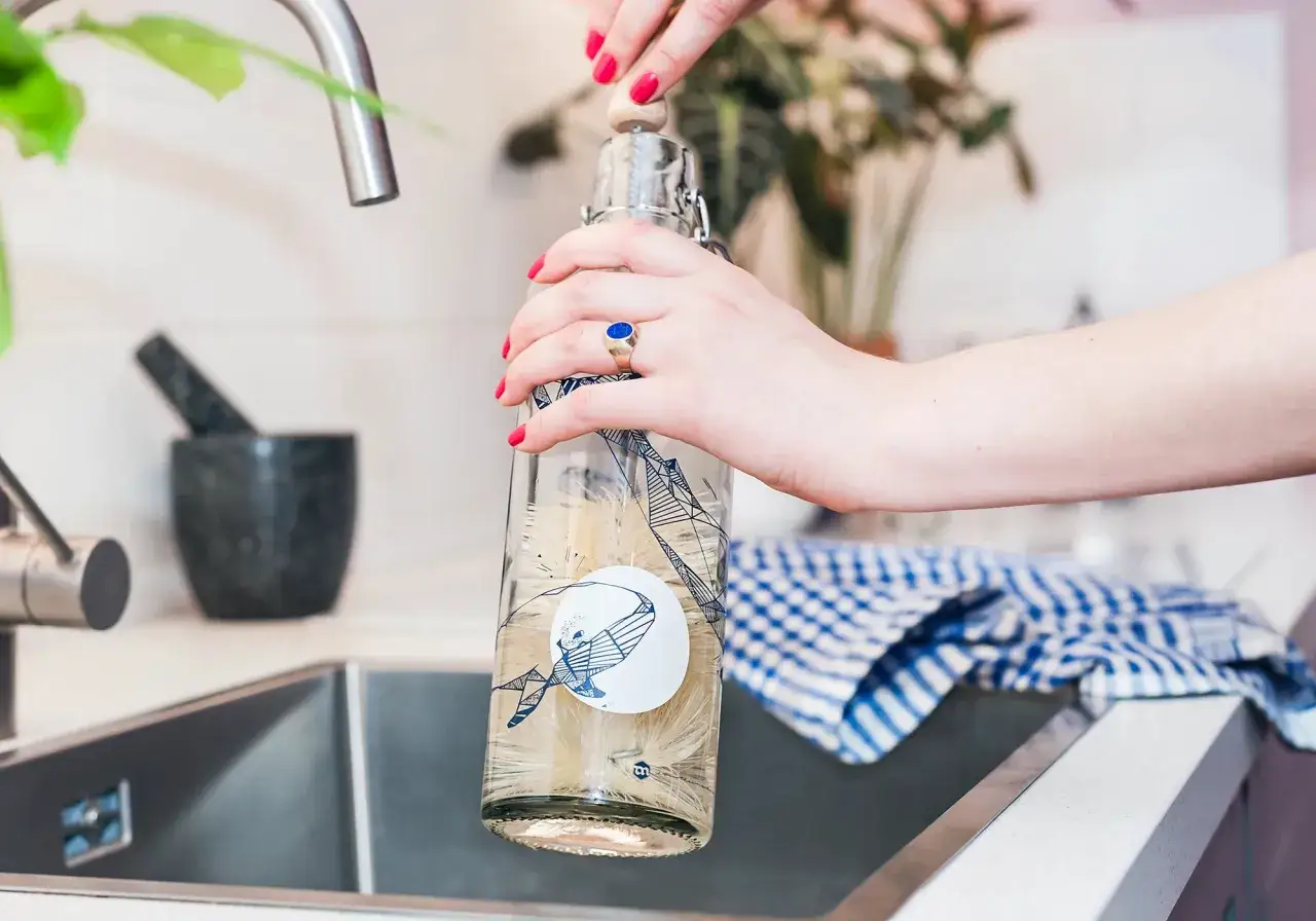 H&auml;nde reinigen eine Trinkflasche mit einer B&uuml;rste. Ein blauer Ring ziert den Finger.