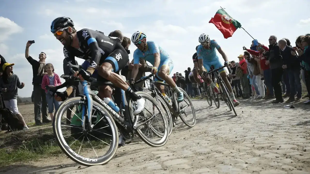 Radprofis k&auml;mpfen auf Kopfsteinpflaster, ein Portugiesisches Flagge weht. Ein Moment, der die H&auml;rte und den Ruhm der monumente des Radsports einf&auml;ngt.