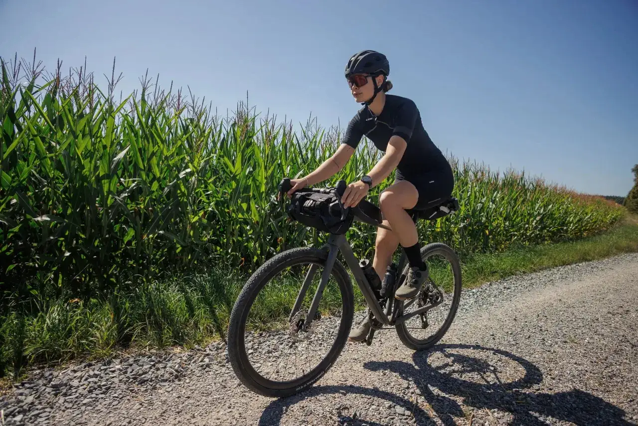 Frau auf Gravelbike genie&szlig;t eine Tour durch Kornfelder.