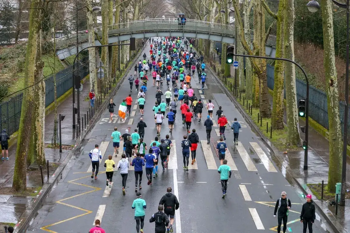 L&auml;ufer beim Semi de Paris auf einer von B&auml;umen ges&auml;umten Stra&szlig;e unter einer Fu&szlig;g&auml;ngerbr&uuml;cke.