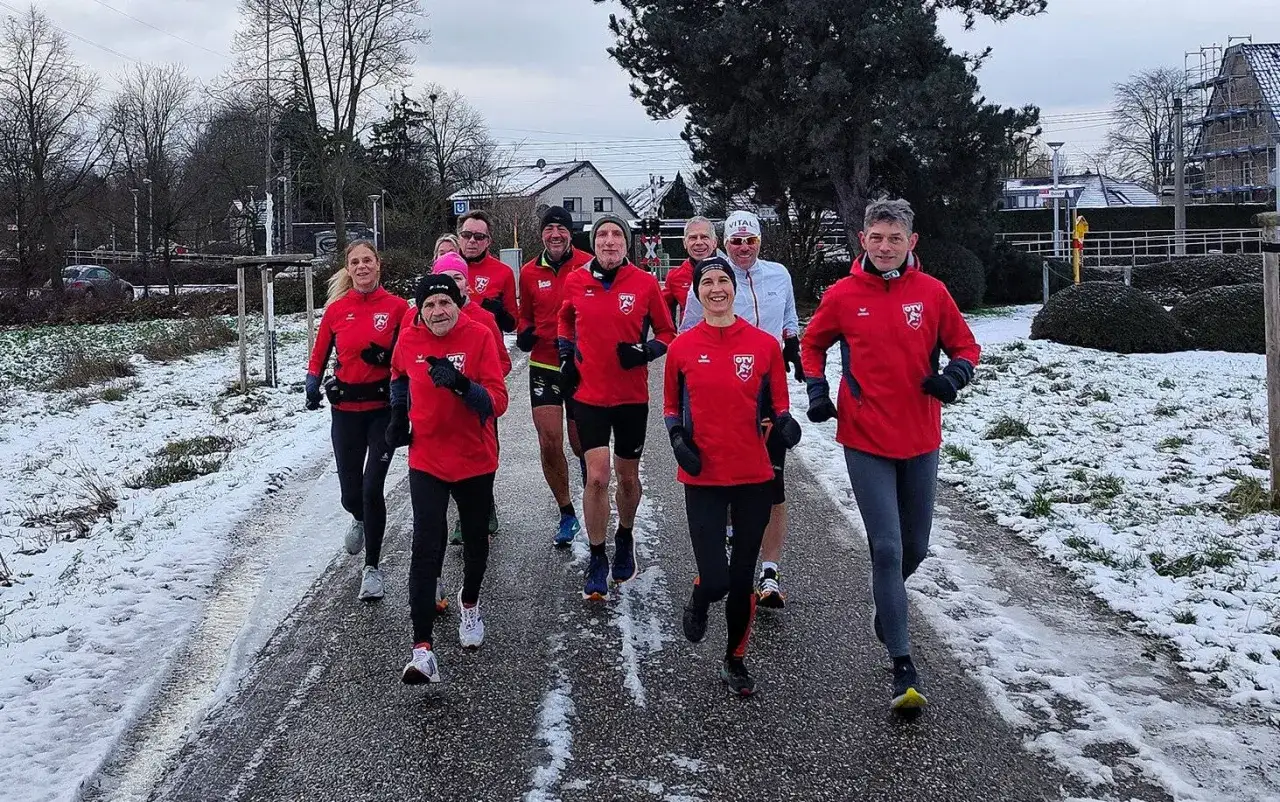 Eine Gruppe L&auml;ufer in roten Trainingsanz&uuml;gen trotzt dem Schnee. Ein fr&ouml;hlicher Tag des Laufens, egal bei welchem Wetter.