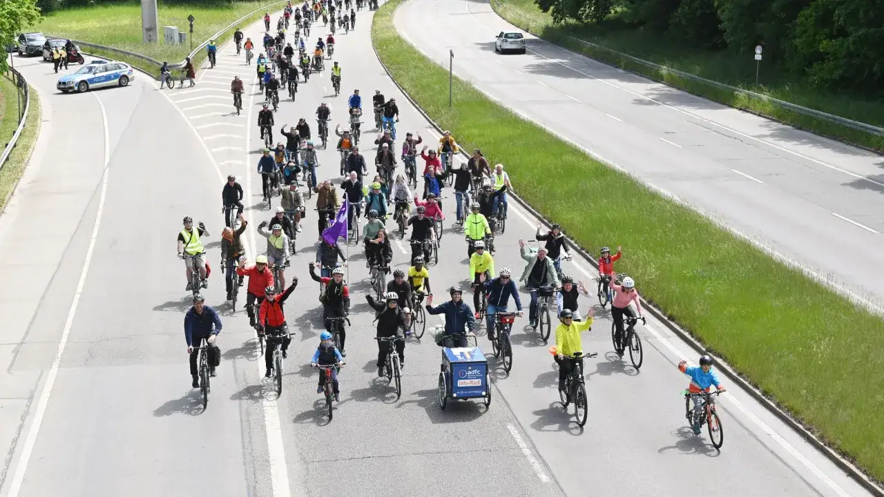 Gro&szlig;e Fahrrad-Community f&auml;hrt gemeinsam auf der Stra&szlig;e. Viele Menschen auf Fahrr&auml;dern, einige winken.
