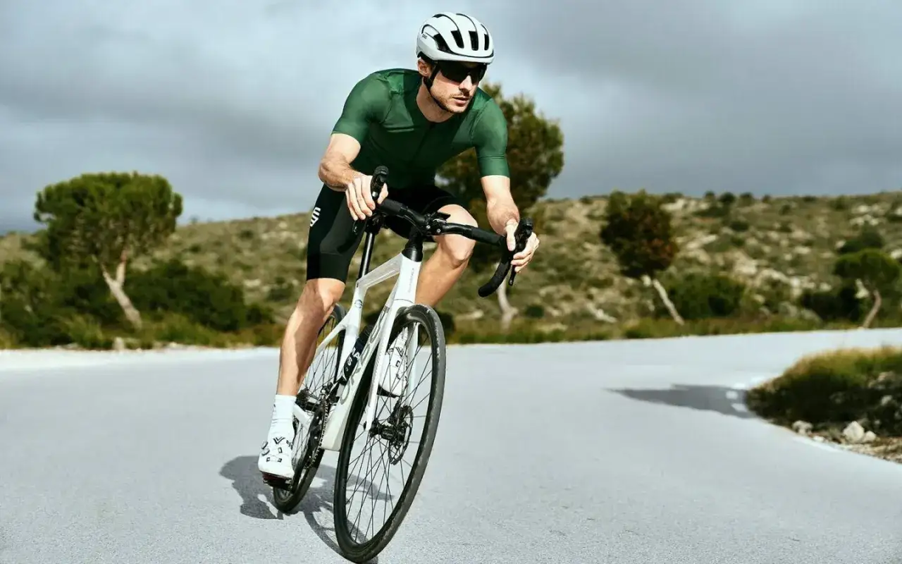 Mann auf Rennrad in gr&uuml;ner Kleidung, mit Helm und Sonnenbrille, auf einer kurvigen Stra&szlig;e. Hier sind einige Rennrad Tipps f&uuml;r deine n&auml;chste Tour.