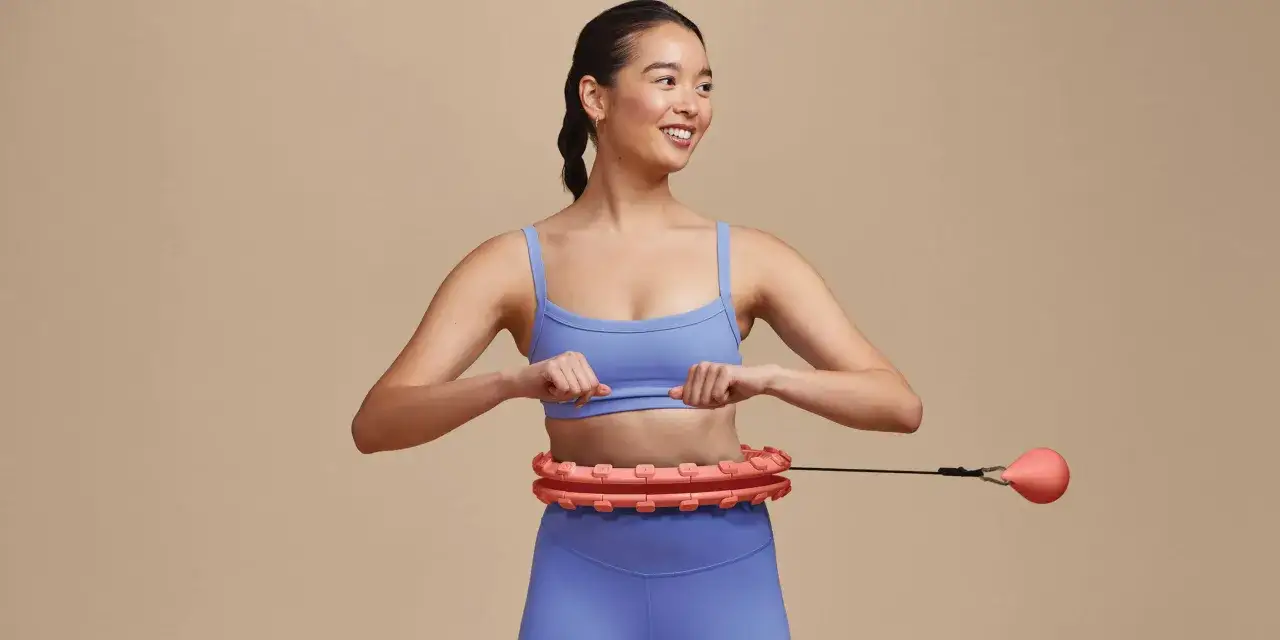 L&auml;chelnde Frau mit Hula Hoop. Entdecke, was Hula Hoop f&uuml;r deine Fitness bringt: Bauchmuskeln st&auml;rken, Kalorien verbrennen und Spa&szlig; haben!