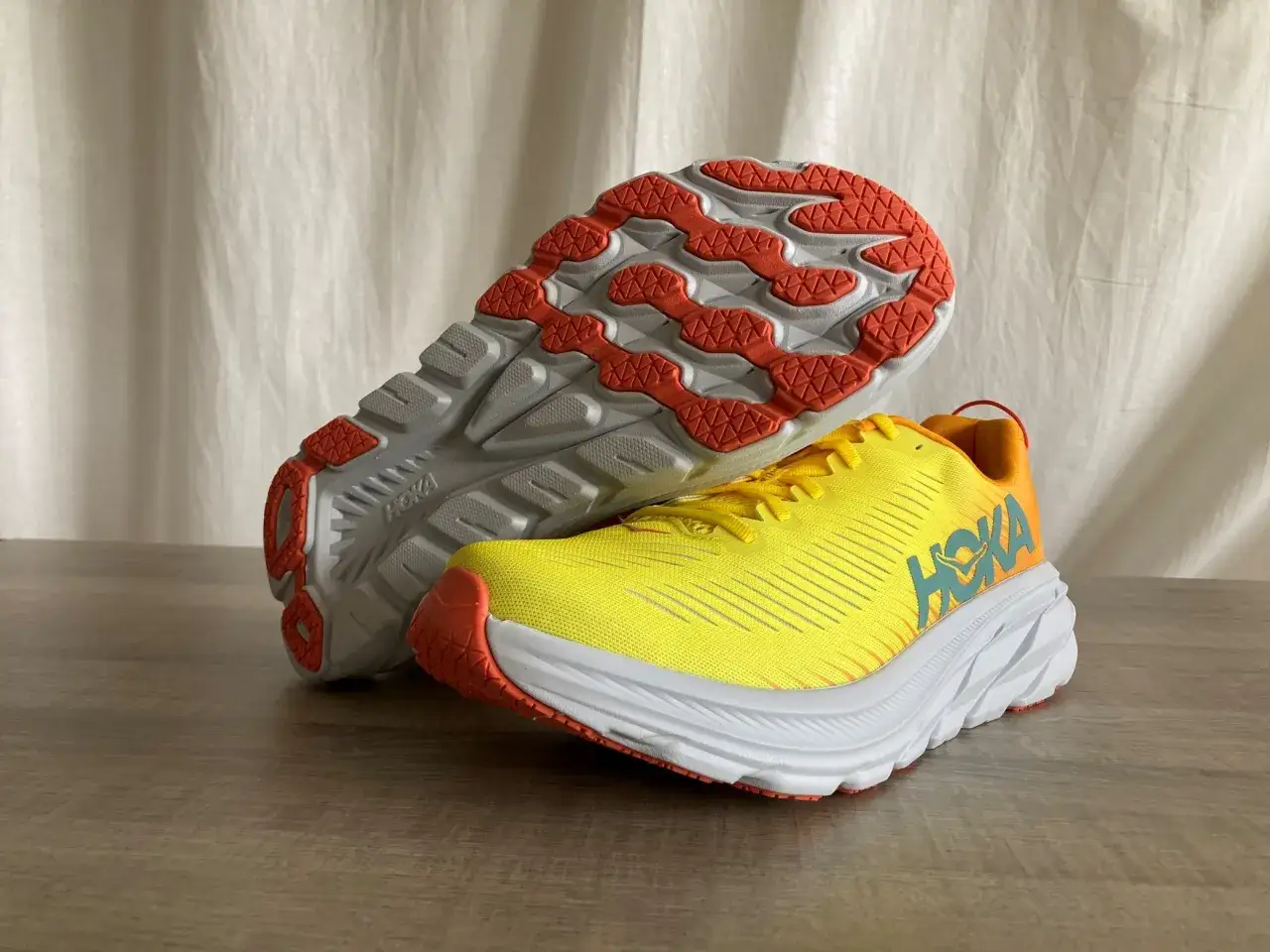 Hoka Rincon 3 Test: Leuchtend gelbe Laufschuhe mit orangefarbenen Akzenten und wei&szlig;er Sohle. Die Sohle zeigt das Hoka-Logo.
