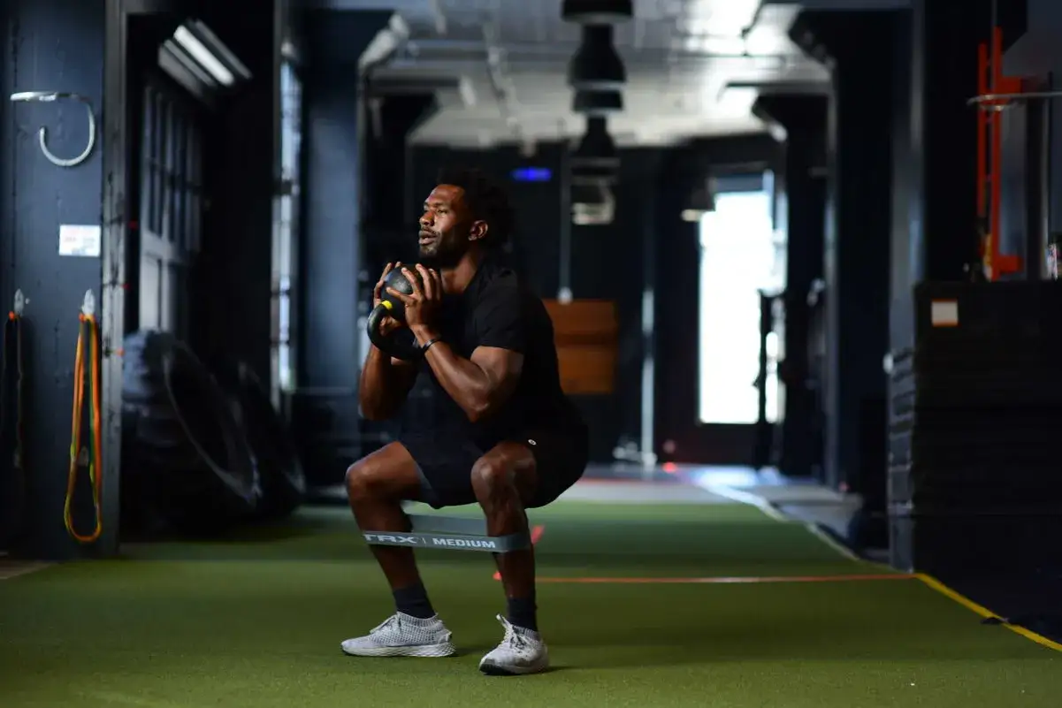 Mann macht Kniebeugen mit Kettlebell und Widerstandsband f&uuml;r starke Kettlebell Beine.