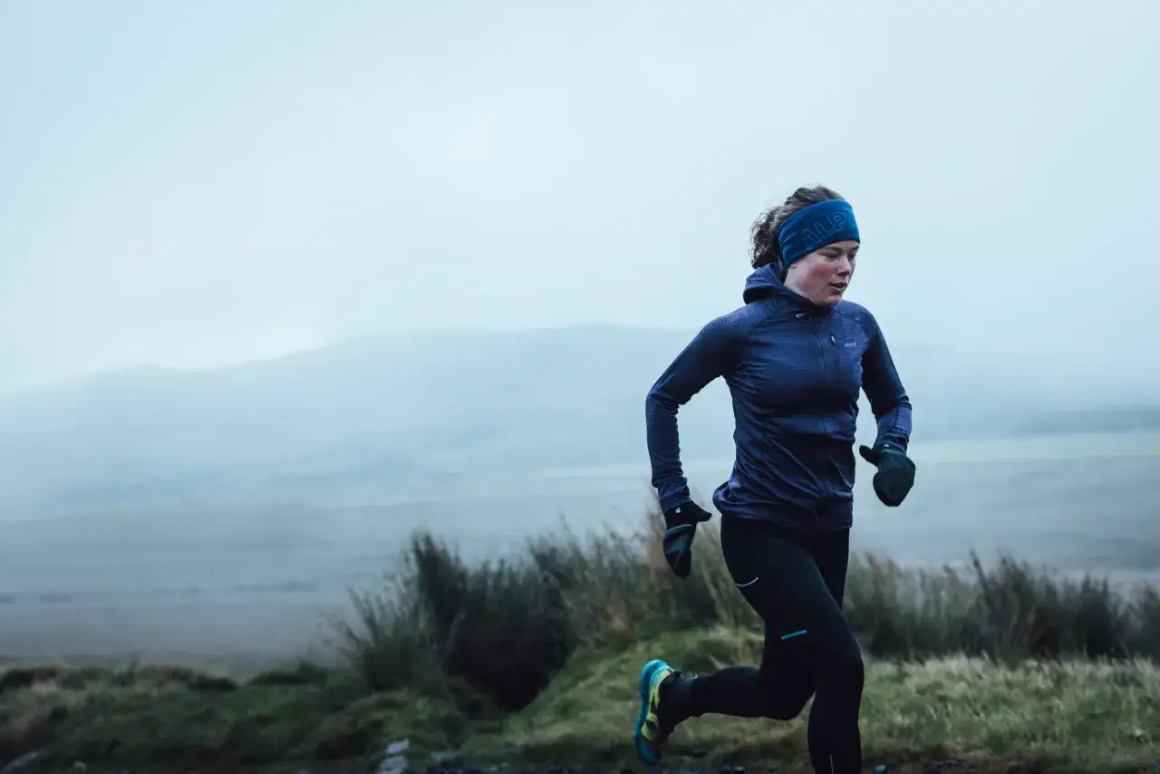 Eine Frau im blauen Stirnband und Laufjacke genie&szlig;t das Trailrunning in nebliger Landschaft.