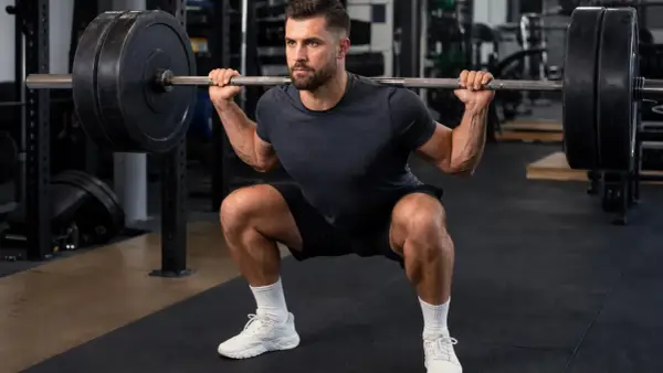 Mann macht Kniebeugen mit Langhantel im Fitnessstudio. Fokus auf Muskelaufbau und Krafttraining.
